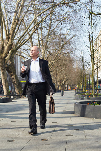 Erwachsener Geschäftsmann  der auf dem Bürgersteig mit Kaffee läuft