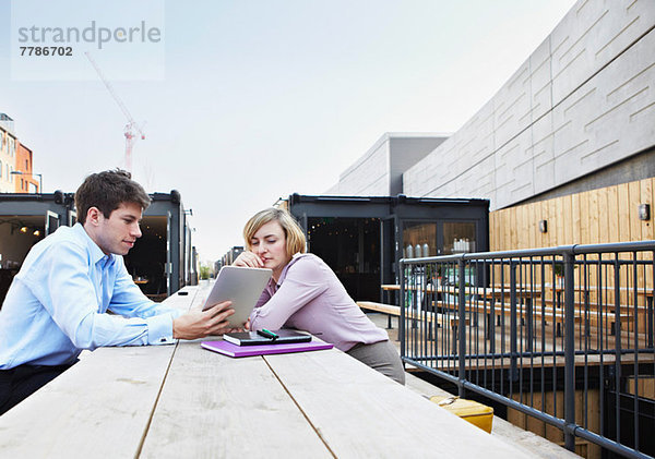 Zwei Personen sitzen am Tisch mit einem digitalen Tablett im Freien.