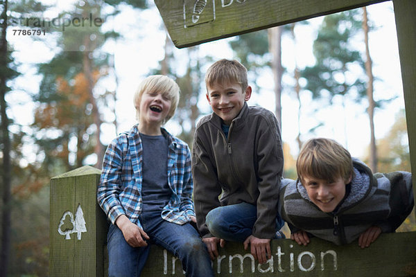 Drei Jungen klettern auf Schild im Wald