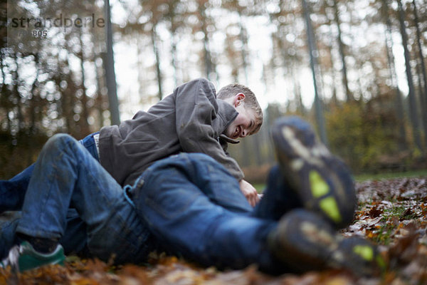 Jungen spielen Kämpfe auf dem Waldboden.