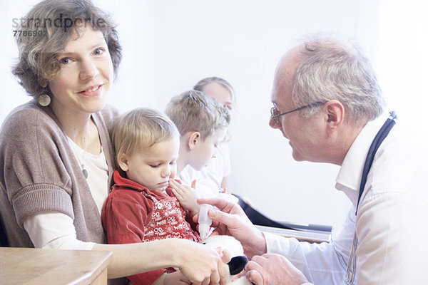 Kind auf dem Schoß der Mutter wird vom Arzt untersucht