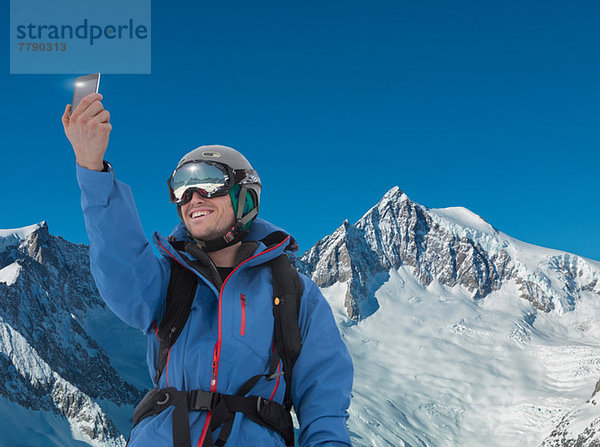 Junger Mann fotografiert sich selbst auf dem Smartphone in den Bergen