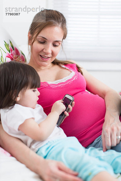 Schwangere Frau und Kleinkind Tochter beim Blick auf das Smartphone