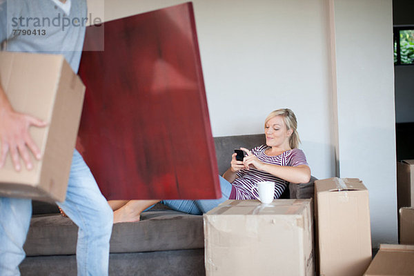 Junge Frau beim Umzug auf Sofa mit Handy