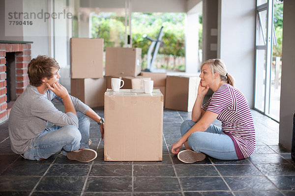 Junges Ehepaar beim Umzug auf dem Boden sitzend mit Kiste