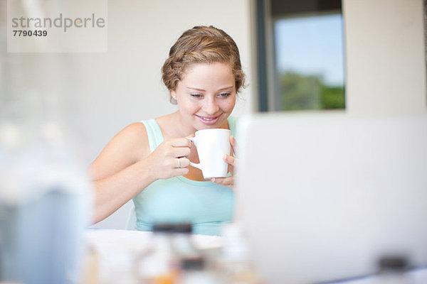 Junge Frau mit Laptop  die Tee trinkt