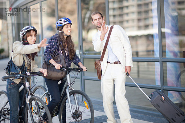 Junge Frauen mit Fahrrädern fragen den jungen Mann nach dem Weg.