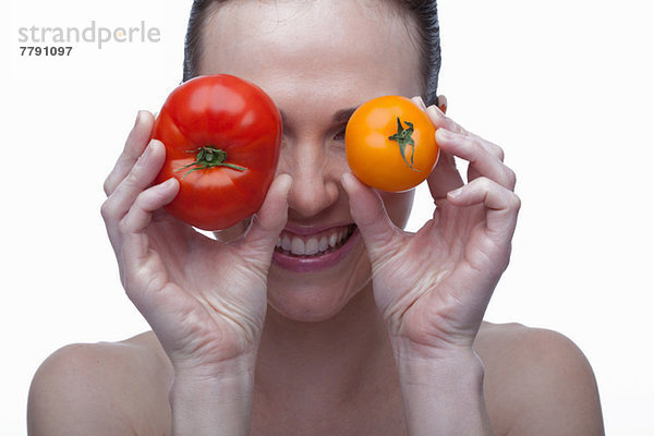 Junge Frau  die die Augen mit roten und gelben Tomaten bedeckt.