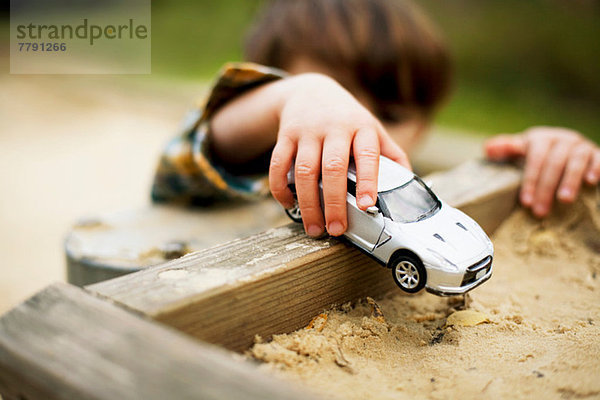 Männliches Kleinkind hält Spielzeugauto über Sandkasten