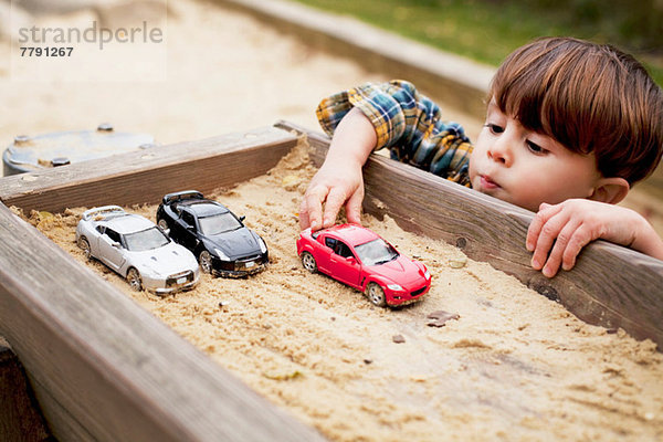 Männliches Kleinkind  das mit Spielzeugautos im Sandkasten spielt