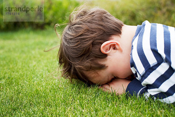Männliches Kleinkind versteckt sich mit dem Gesicht nach unten auf Gras.