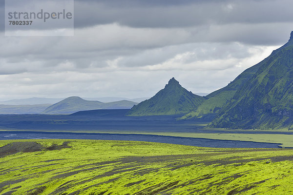 Hügel mit Moos  dahinter schwarze Sandfläche und spitzer Berg  Aussicht von der Straße in die Þakgil