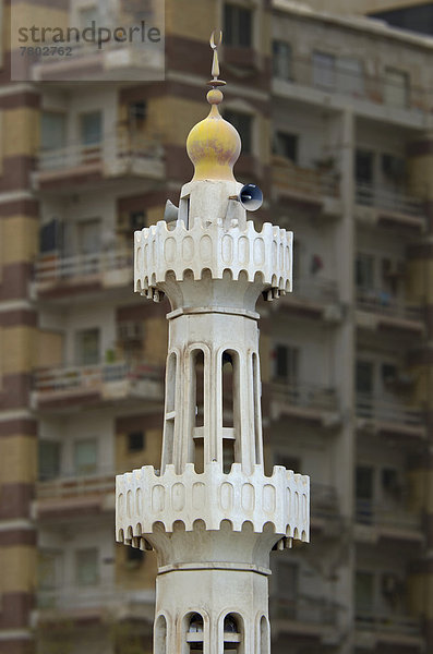 Das Minarett einer kleinen Moschee vor einem Mehrfamilienhaus mit Balkons