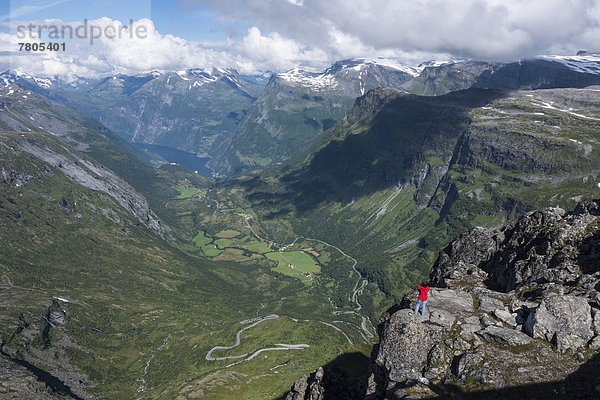 Tourist steht auf einem Felsen auf dem Berg Dalsnibba  1495m  hinten der Geirangerfjord