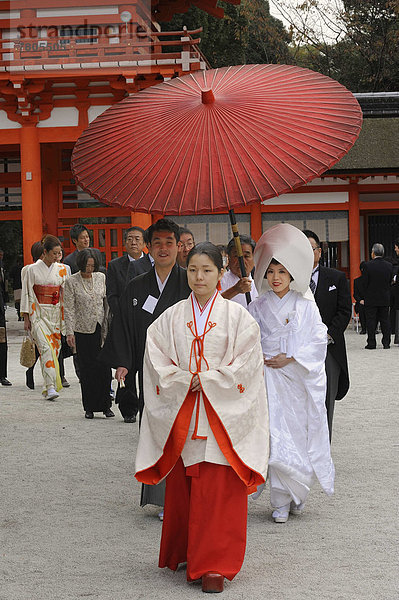 Japanerin mit scharlachroter Hakama-Hose und einem weißen Kimono-Hemd mit weiten Ärmeln  vor dem Torhaus  Shimogamo-Schrein