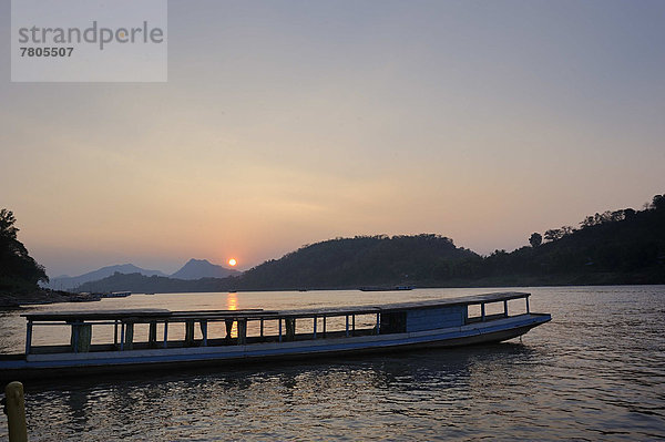 Abendstimmung mit Sonnenuntergang über dem Mekong und im Vordergrund ein Passagierboot