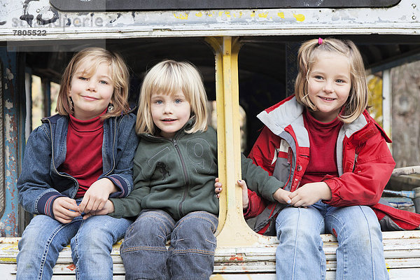 Drei Kinder sitzen in einem ausrangierten Bus