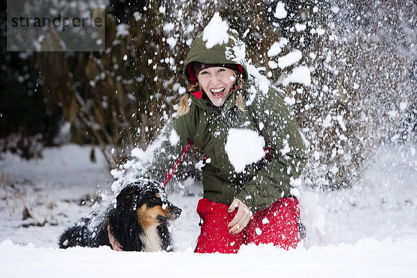 Junge Frau spielt mit Australian Shepherd im Schnee