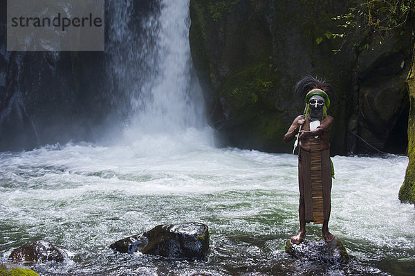 Geschmückter und bemalter Stammeschef steht vor einem Wasserfall im Hochland