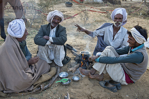 Vier Inder mit Turbanen sitzen am Boden und unterhalten sich  auf einem Feuer wird Milchtee zubereitet  Kamelmarkt