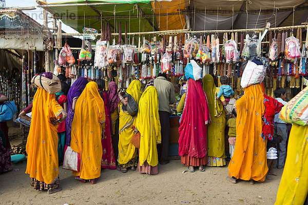 Inderinnen in bunten Saris stehen vor einem Verkaufsstand für Spielsachen und Modeschmuck  Kamelmarkt