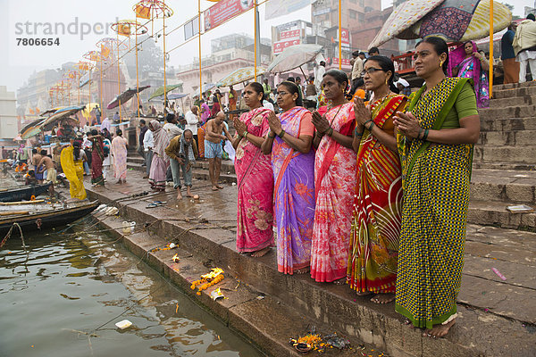 Fünf Frauen in bunten Saris stehen betend am Gangesufer