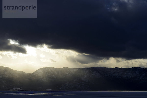 Sonne bricht durch die Wolken am zugefrorenen See Kussharo Lake