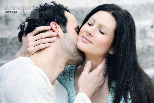 Junger Mann küsst junge Frau am Hals