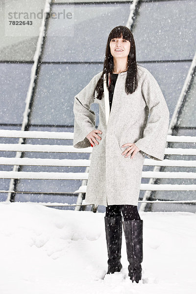 Junge Frau mit Mantel steht im Schnee