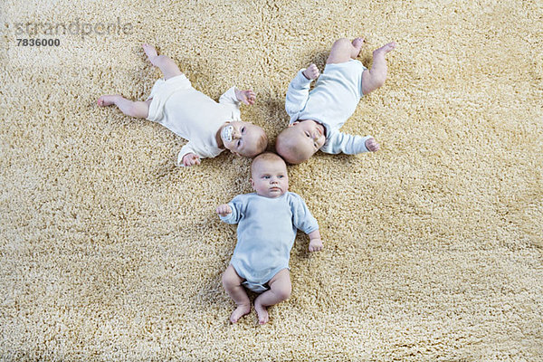Bildung von drei Babys  die auf einem Teppich liegen.