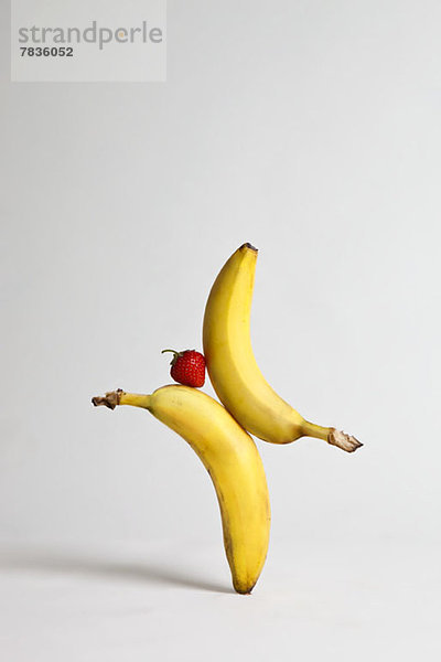 Eine Erdbeere  die zwischen zwei Bananen balanciert.