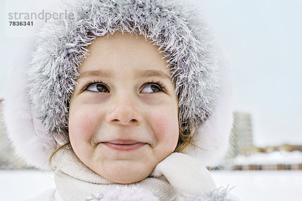 Ein schelmisch lächelndes junges Mädchen  das im Winter draußen einen Pelzhut trägt