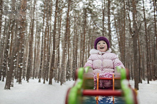 Ein junges fröhliches Mädchen auf einem Spielplatzgerät im Winter