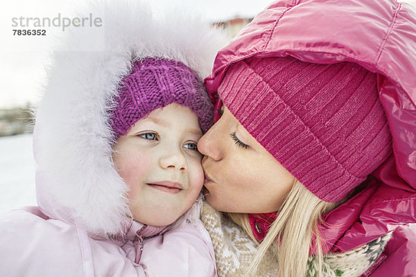 Eine Mutter  die ihre Tochter im Winter draußen küsst.