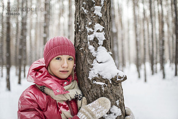 Eine Frau in warmer Kleidung  die im Winter neben einem Baum posiert.