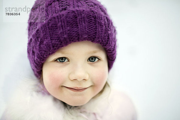 Ein junges lächelndes Mädchen mit Strickmütze  im Winter im Freien