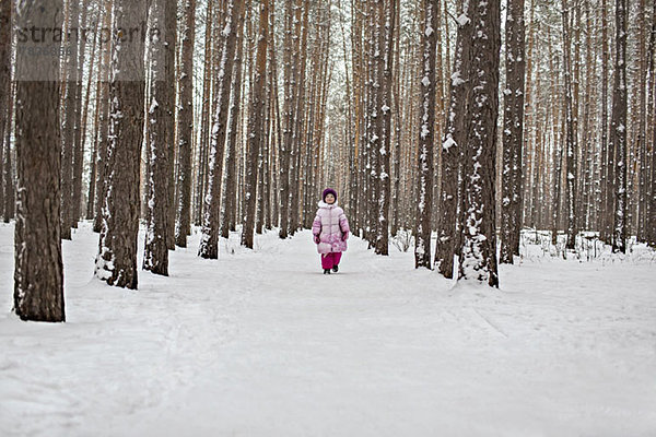 Ein junges Mädchen  das einen schneebedeckten Pfad im Wald hinuntergeht.