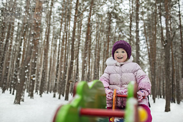 Ein junges fröhliches Mädchen auf einem Spielplatzgerät im Winter