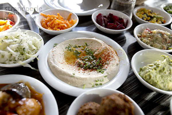 Ein Teller mit garniertem Hummus auf dem Tisch  umgeben von verschiedenen Salaten.