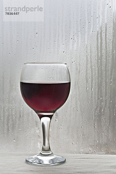Glas Rotwein durch regenbedecktes Fenster