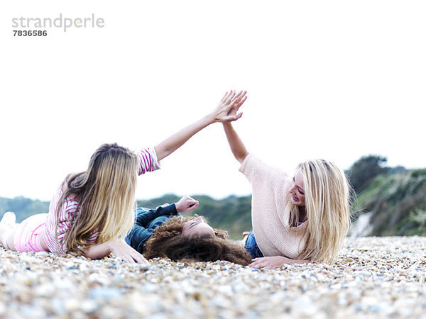 Ein Mädchen  das zwischen zwei Freunden liegt und am Strand über ihr liegt.