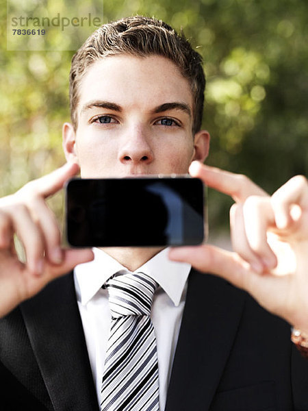 Ein junger Geschäftsmann hält sein Smartphone vor den Mund.