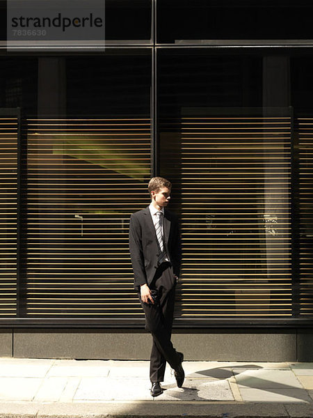 Ein junger Geschäftsmann steht vor einem Gebäude und schaut weg.