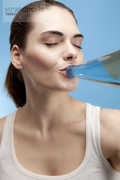 Eine zufriedene junge Frau trinkt Wasser aus einer Glasflasche.