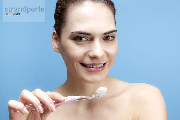 Eine lächelnde junge Frau hält eine Zahnbürste mit Zahnpasta darauf.