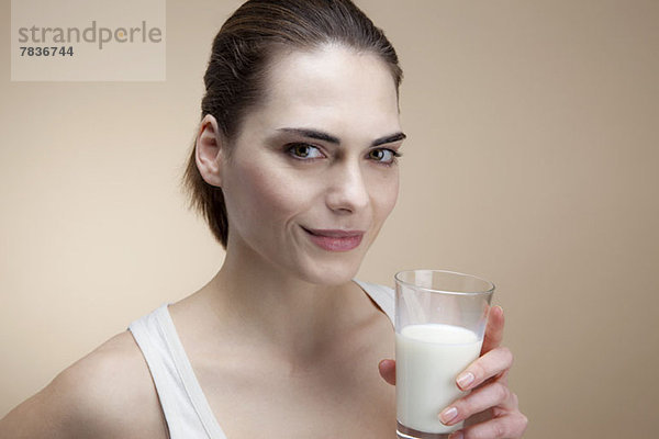 Eine lächelnde junge Frau hält ein Glas Milch.