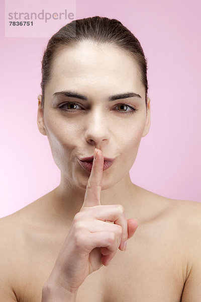 Eine junge Frau  die ihren Finger spielerisch auf die Lippen legt  den Mund.