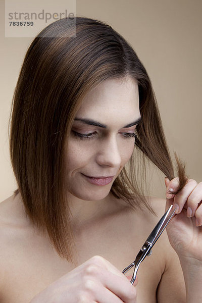Eine lächelnde junge Frau  die sich konzentriert  während sie ihr eigenes Haar schneidet.