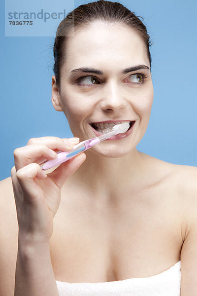 Eine lächelnde junge Frau  die sich die Zähne putzt  während sie nachdenklich wegschaut.