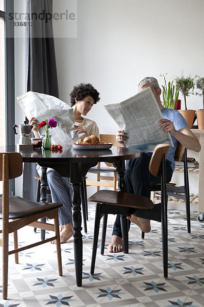 Ein angesagtes  gemischtes Ehepaar  das Zeitungen liest und frühstückt.
